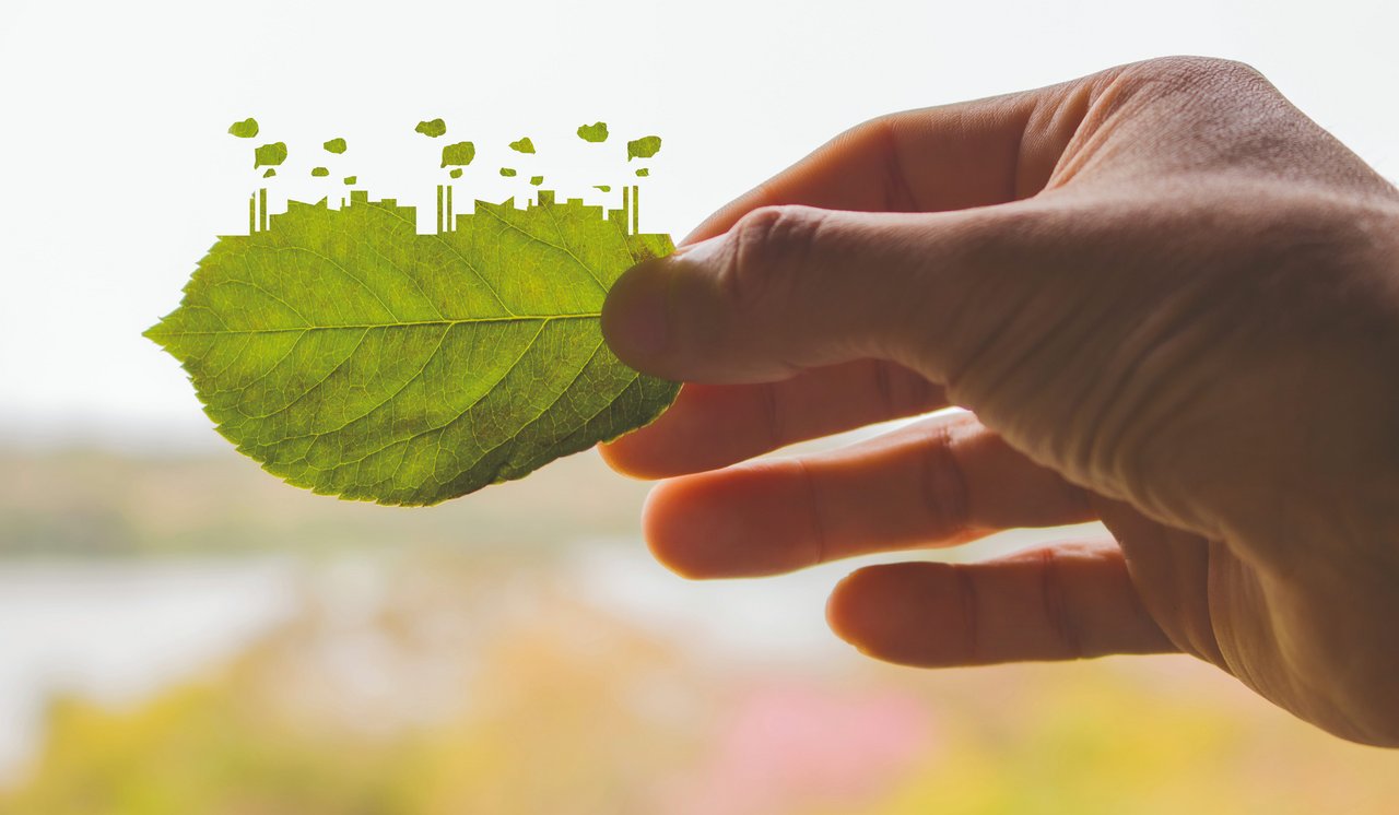Symbolbild: eine Hand hält ein Laubblatt, das auf einer Seite die Umrisse einer Industrielandschaft hat