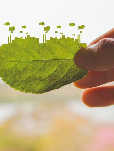Symbolbild: eine Hand hält ein Laubblatt, das auf einer Seite die Umrisse einer Industrielandschaft hat