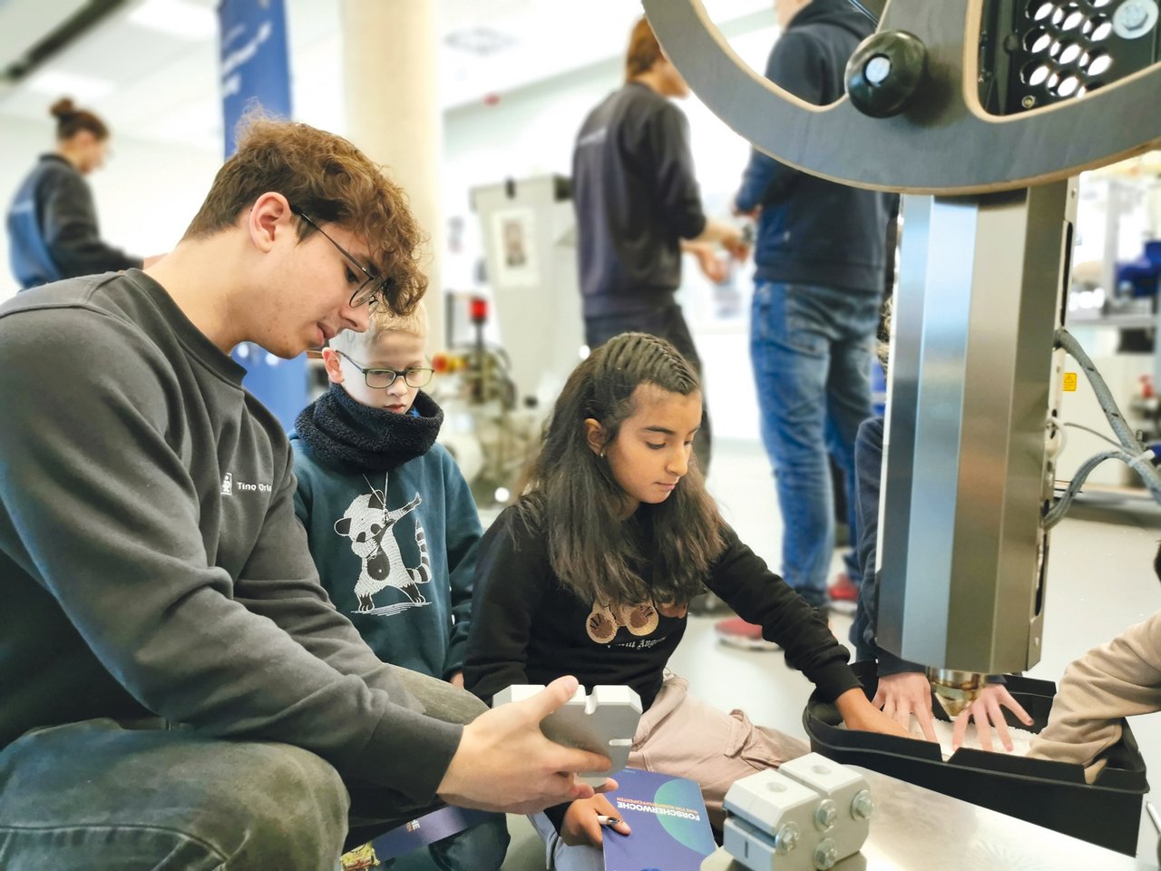 Foto von Azubis, die Kindern das Zukunftsmobil zeigen
