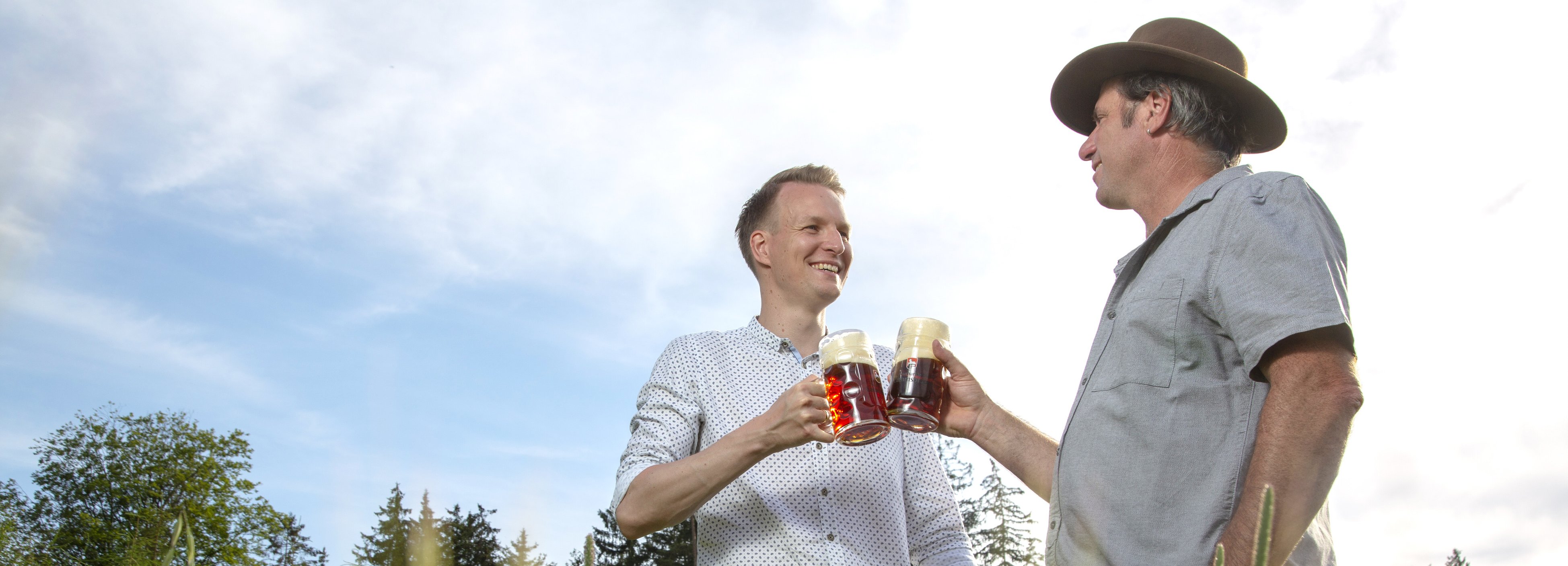 Zwei Männer stoßen mit vollen Biergläsern auf einer Wiese miteinander an