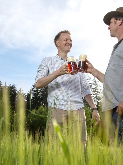 Zwei Männer stoßen mit vollen Biergläsern auf einer Wiese miteinander an