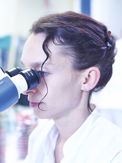 Foto einer Frau, die durch ein Mikroskop sieht