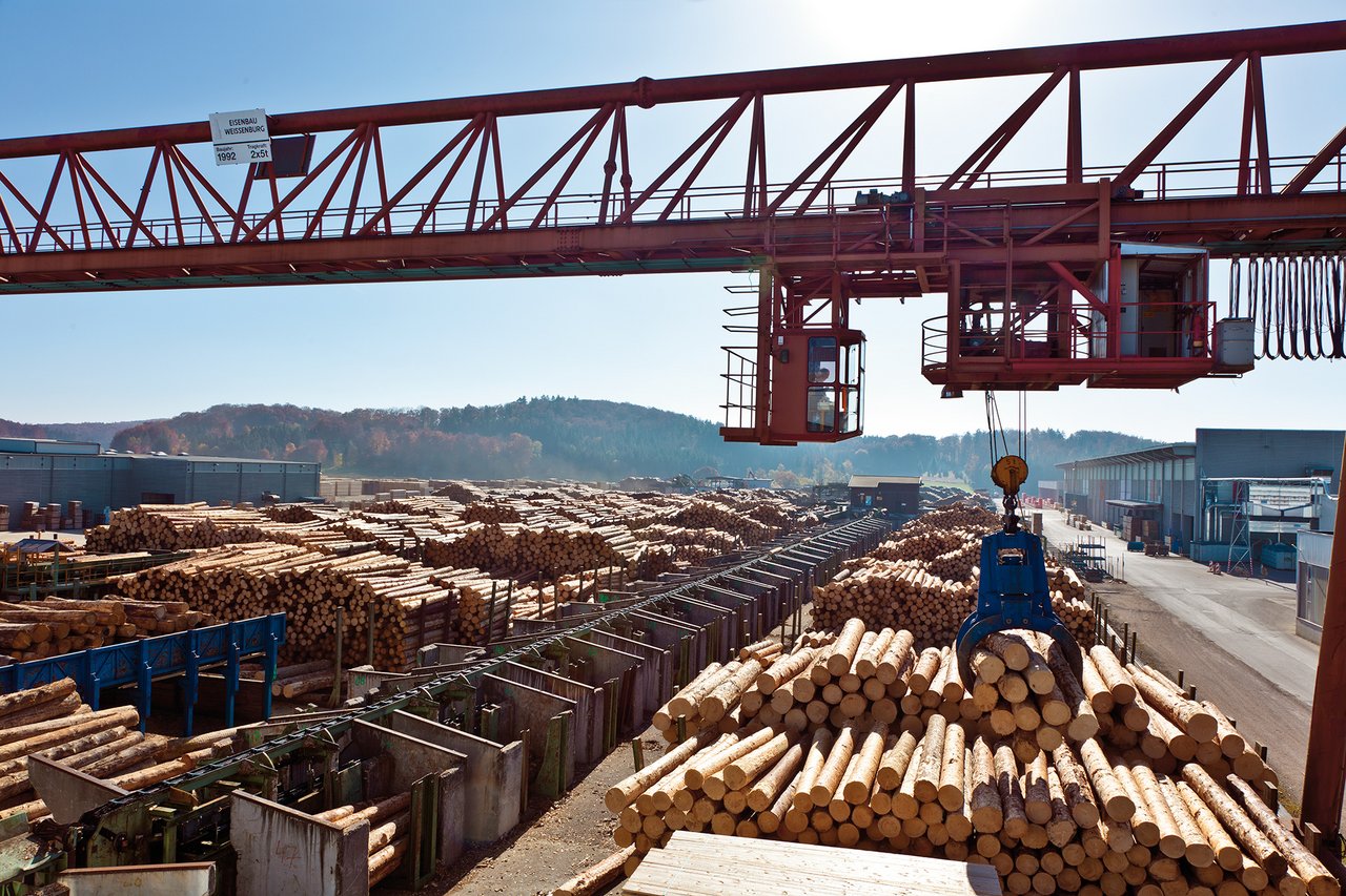 Foto von einem Kran, der Baumstämme auf einem Holzlagerplatz bewegt